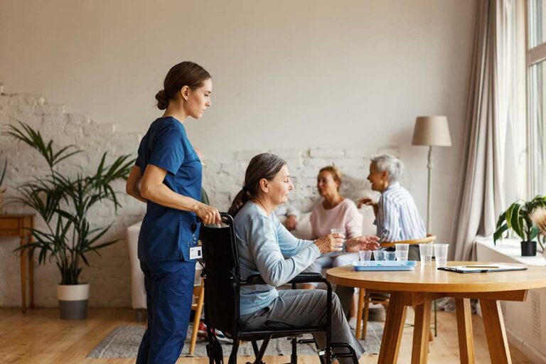 Staff member helps an older resident clean hands in a bright assisted living common area.